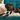 Black dog lying on a teal couch with a white toy, wearing a beige blanket and a Beco Tough Tugger Dog Toy